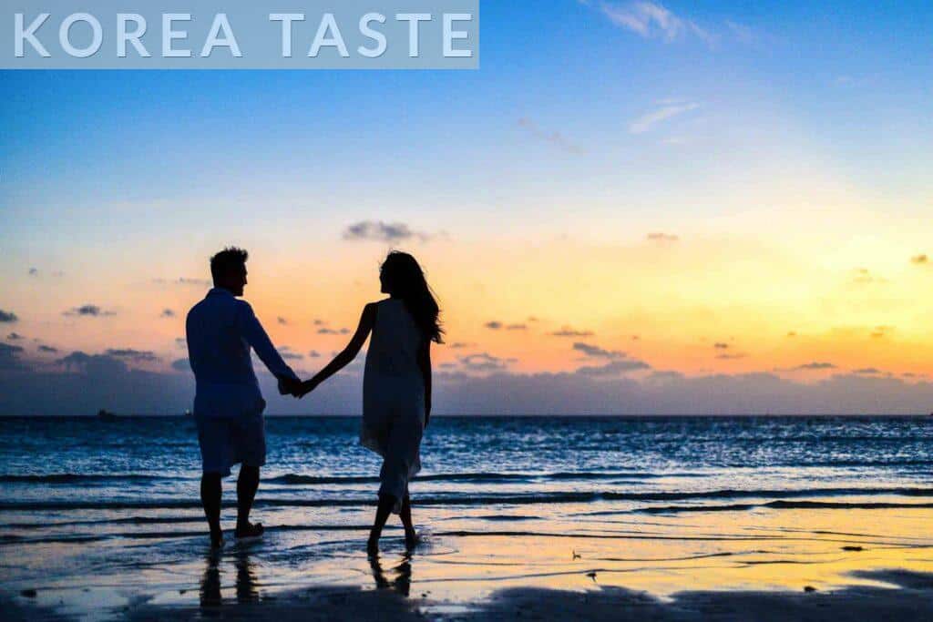 Man and Woman Holding Hands Walking on Seashore during Sunrise